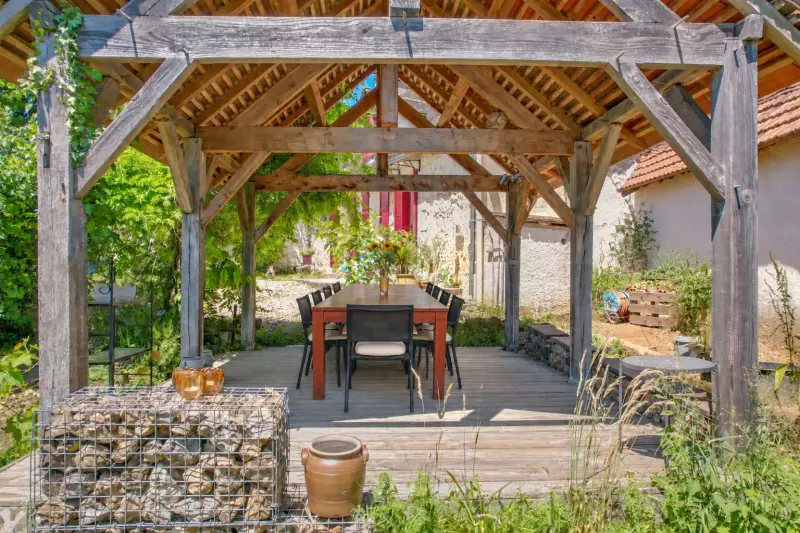 De overdekte pergola met eettafel en stoelen, in het groen naast het huis